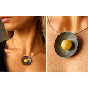 Op de afbeelding: Een zilveren ketting met een ronde hanger met een gele bol in het midden.
