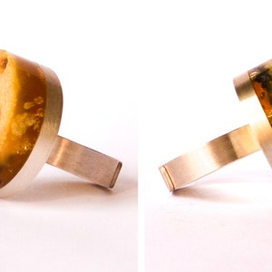May include: A silver ring with a large, amber-colored stone set in the center. The stone has a natural, organic look with swirls and inclusions.