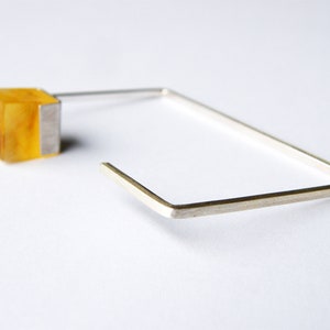 May include: A silver square hoop earring with a yellow amber cube attached to the top.