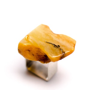 May include: A yellow amber ring with a silver band. The amber is a natural stone with a unique shape and texture.