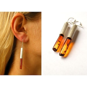 Puede incluir: Un par de pendientes de plata con piedras de ámbar. Las piedras de ámbar son transparentes y tienen un color marrón. Los pendientes miden aproximadamente 5 cm de largo.