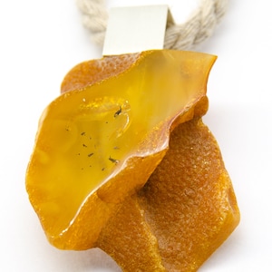 Pode incluir: Um grande pingente de &acirc;mbar de forma irregular com uma argola de prata, pendurado em uma corda de fibra natural.