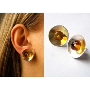 Puede incluir: Un par de pendientes de plata con piedras de ámbar engastadas en un metal dorado. Los pendientes son redondos y tienen una forma ligeramente abovedada.