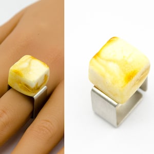 Könnte beinhalten: Ein quadratischer Ring mit einem gelben Bernstein, der in eine silberne Fassung gefasst ist.