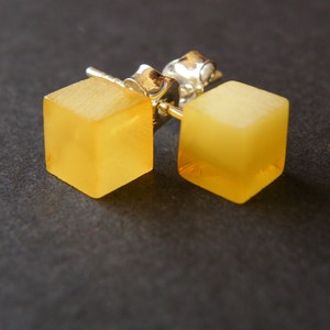 Puede incluir: Un par de pendientes de cubo de ámbar con postes de plata. Los pendientes son de color amarillo claro y tienen un acabado liso y pulido.