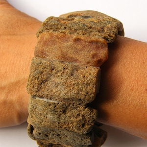 Könnte beinhalten: Ein massives Bernstein-Armband aus übereinander gestapelten, unregelmäßigen Bernsteinstücken. Der Bernstein hat eine Mischung aus braunen, orangen und gelben Tönen.
