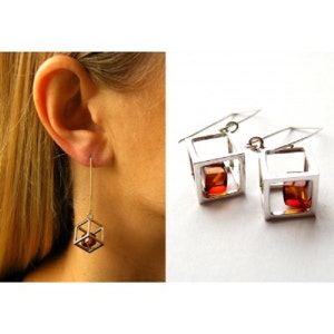 Puede incluir: Pendientes de plata con una piedra de ámbar en forma de cubo dentro de cada cubo.