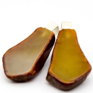 Puede incluir: Dos colgantes de ámbar con baúles de plata. Un colgante es de color ámbar claro y el otro es de color ámbar oscuro.