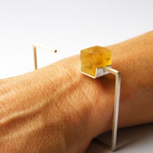 May include: A silver bracelet with a clear, yellow, cube-shaped stone. The bracelet is open and has a simple, geometric design.