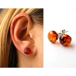Puede incluir: Un par de pendientes de botón de ámbar con postes de plata. Los pendientes son redondos y tienen un acabado liso y pulido. El ámbar es de un color rico y cálido.
