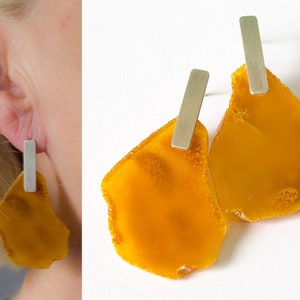 Puede incluir: Un par de pendientes de ámbar con postes de barra de plata. El ámbar es de un color miel cálido y tiene una forma natural irregular.