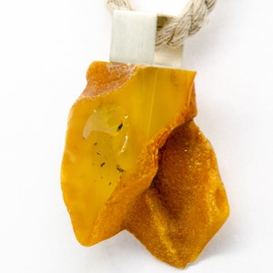 Pode incluir: Um pingente de &acirc;mbar amarelo com uma argola de prata, pendurado em uma corda de fibra natural.
