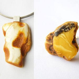 May include: Two amber pendants, one on a silver chain and one on a silver ring. The amber is a mix of white and yellow with brown inclusions.