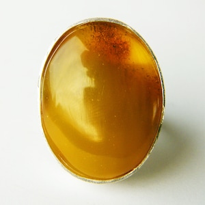 May include: A silver ring with a large oval amber stone. The amber is a deep yellow color and has a few inclusions.