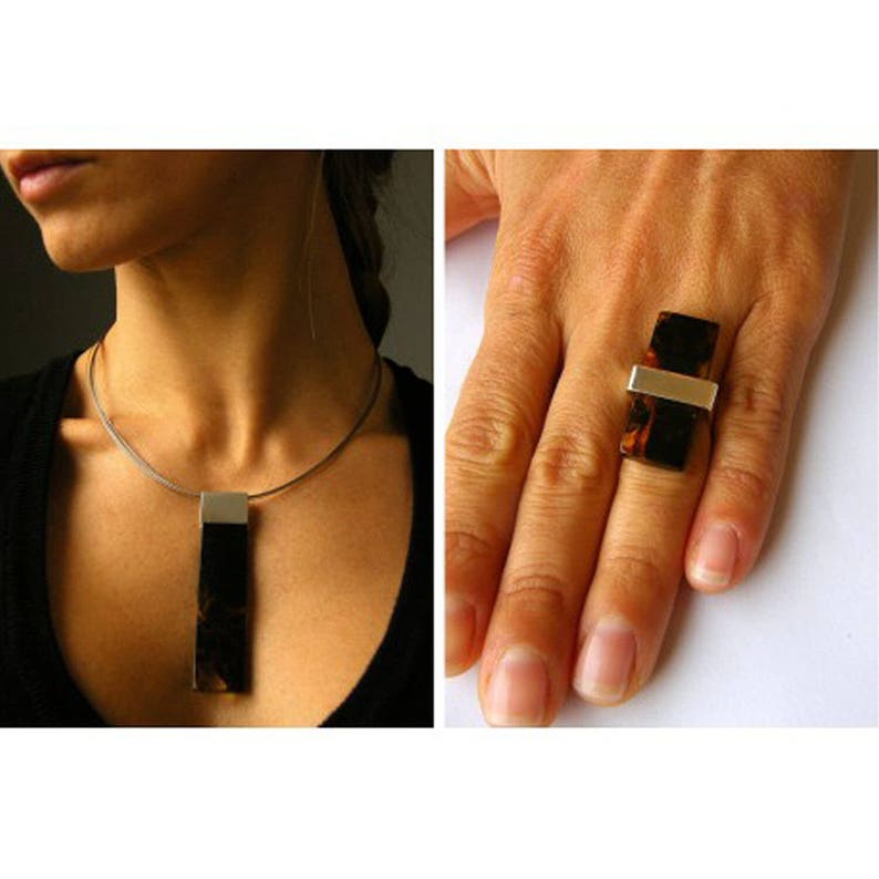 May include: A silver necklace with a brown and silver pendant. A matching ring with a brown and silver stone is on a finger.