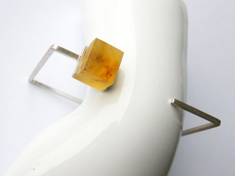 May include: A silver geometric ring with a clear amber cube in the center.