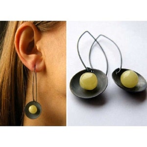 Puede incluir: Un par de pendientes colgantes con una cuenta de vidrio amarilla y un disco de metal negro.