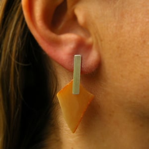 Puede incluir: Un par de pendientes con una piedra de ámbar geométrica en forma de diamante y un colgante de barra de plata.