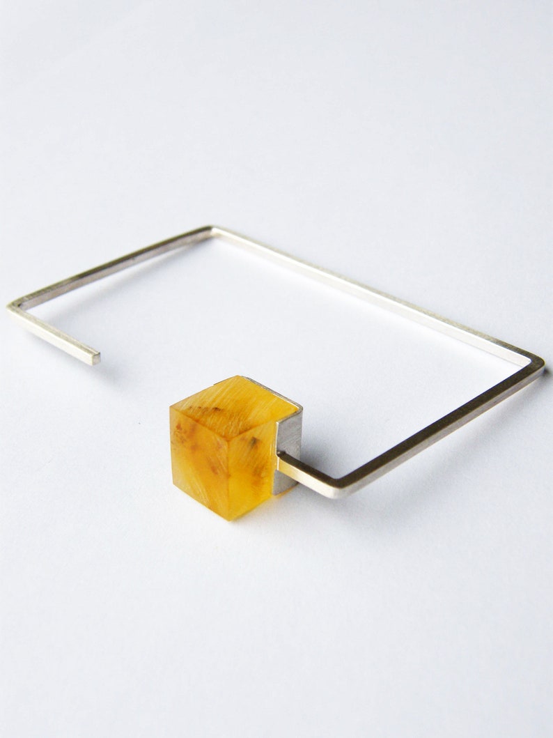 May include: A silver bracelet with a square amber-colored stone attached to it.