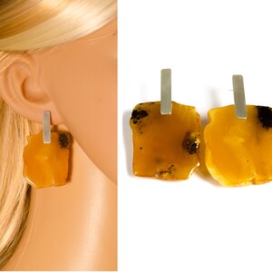 May include: A pair of amber earrings with silver posts. The amber is a warm, honey color and has a natural, irregular shape. The earrings are a statement piece and would be perfect for a special occasion.
