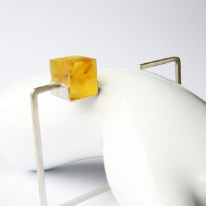 May include: A silver ring with a square amber stone set in the center. The ring is on a white surface.