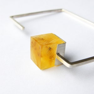 May include: A silver bracelet with a clear yellow cube-shaped charm. The charm has a silver frame.