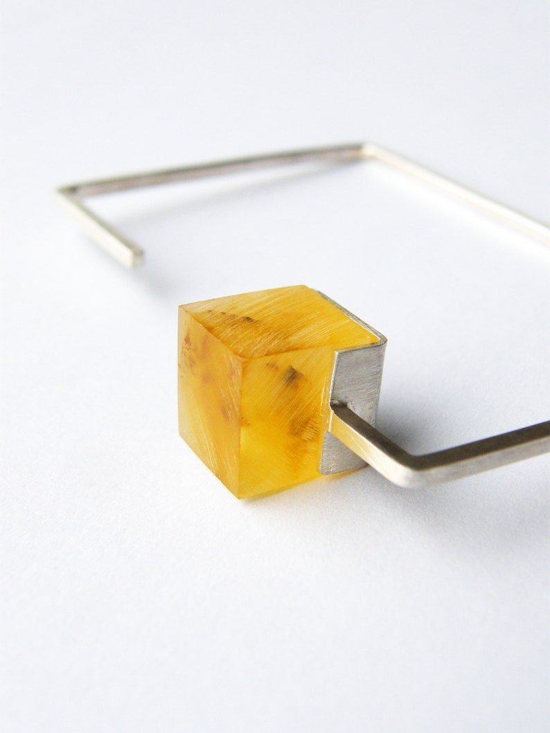 May include: A silver bracelet with a clear yellow cube-shaped charm. The charm has a silver frame.