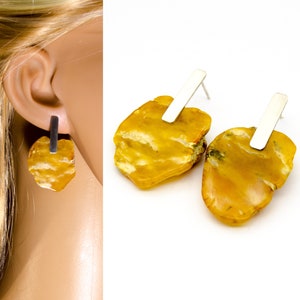 Puede incluir: Un par de pendientes de ámbar con postes de plata. El ámbar es de color amarillo cálido y tiene una forma natural irregular. Los pendientes son una pieza llamativa y serían una gran adición a cualquier colección de joyas.