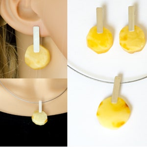 May include: A set of amber earrings and a necklace with silver accents. The amber stones are round and have a yellow color. The silver accents are rectangular.