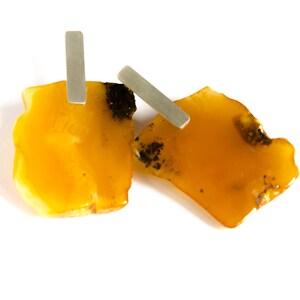 May include: A pair of amber earrings with silver accents. The amber is a warm, honey color and has a natural, irregular shape. The silver accents are simple and elegant.