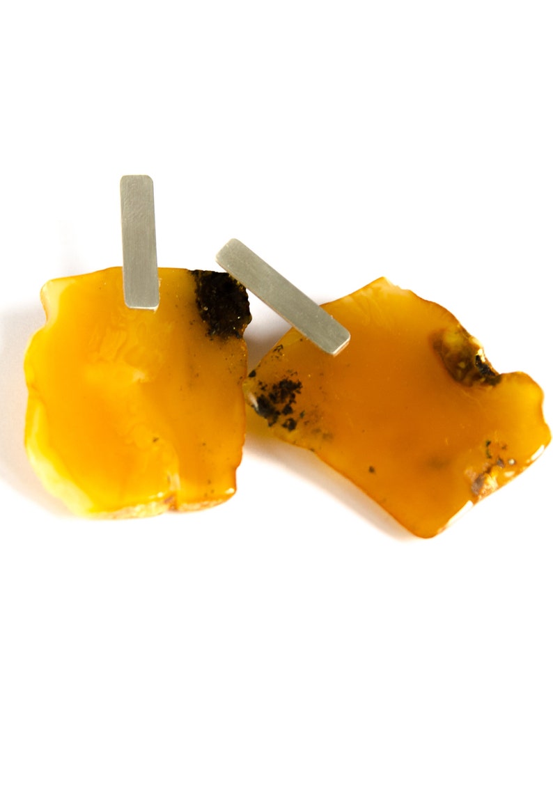 May include: A pair of amber earrings with silver accents. The amber is a warm, honey color and has a natural, irregular shape. The silver accents are simple and elegant.