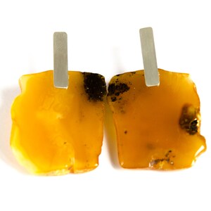 May include: A pair of amber earrings with silver posts. The amber is a warm yellow color with dark brown inclusions.