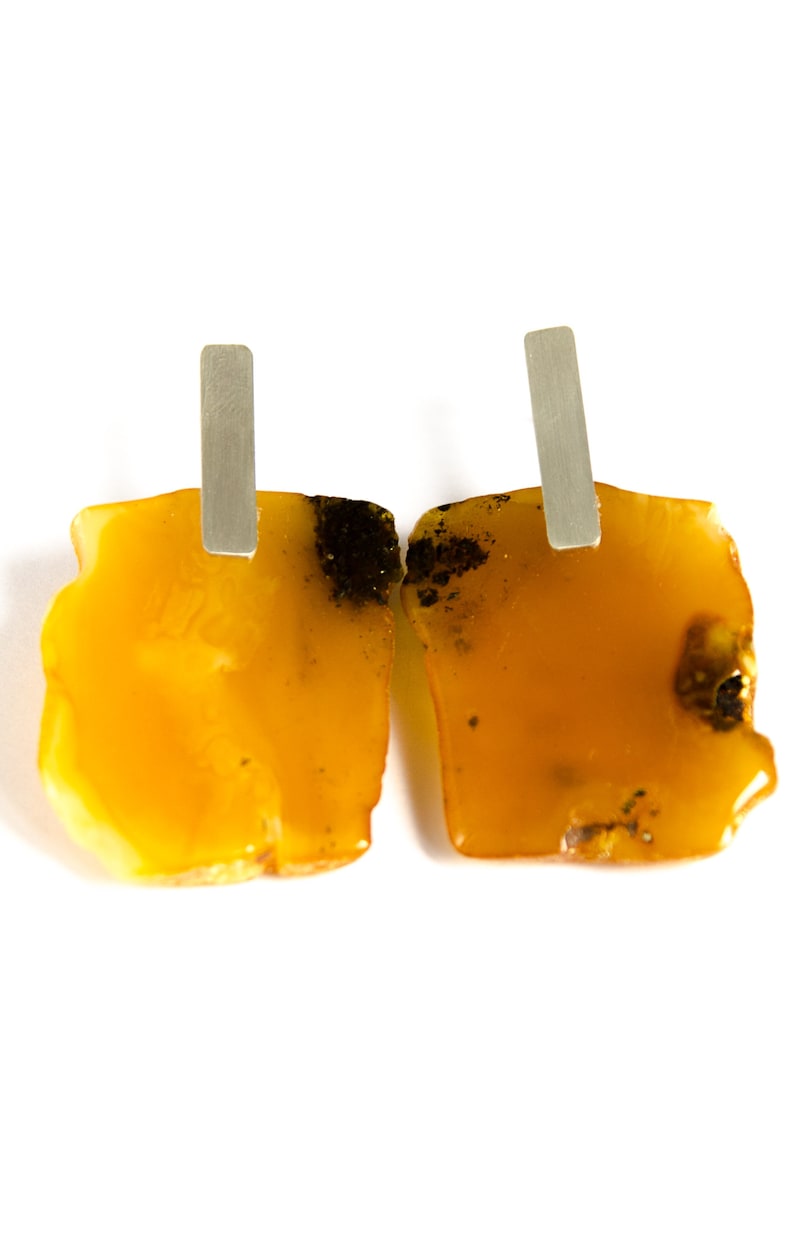 May include: A pair of amber earrings with silver posts. The amber is a warm yellow color with dark brown inclusions.