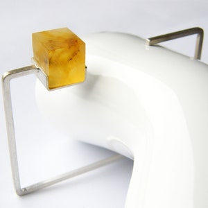 May include: A silver ring with a square amber stone set in a geometric frame.
