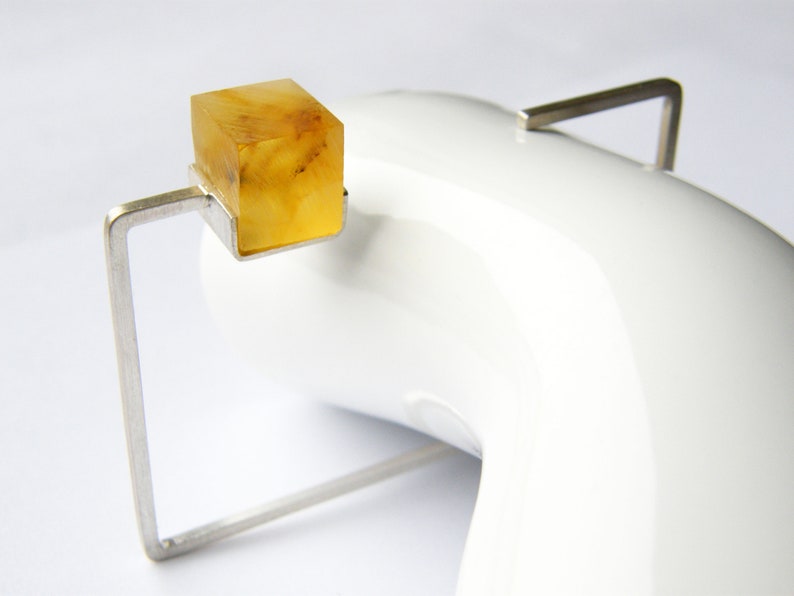May include: A silver ring with a square amber stone set in a geometric frame.