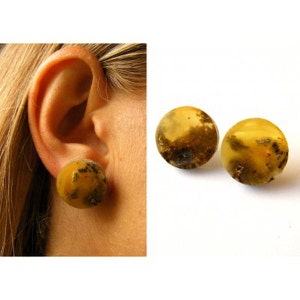 Puede incluir: Un par de pendientes de ámbar con un aspecto moteado y nublado. Los pendientes son redondos y tienen un color amarillo dorado.