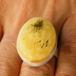 May include: A silver ring with a large oval amber stone. The amber is a pale yellow color with black inclusions.
