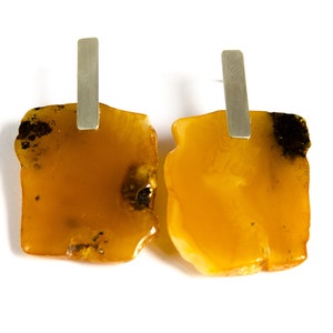 May include: A pair of amber earrings with silver posts. The amber is a warm, honey color and has a natural, irregular shape.