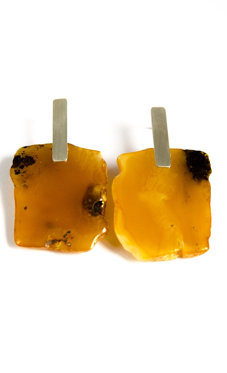 May include: A pair of amber earrings with silver posts. The amber is a warm, honey color and has a natural, irregular shape.