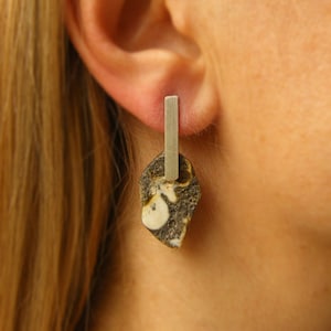 Puede incluir: Pendientes de plata con un colgante de piedra negra y blanca. La piedra tiene un patrón único y está unida a una barra de plata.