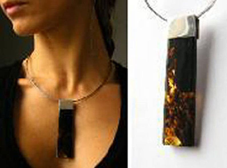 May include: A silver chain necklace with a rectangular pendant featuring a dark amber stone with gold flecks.