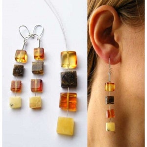 Puede incluir: Un par de pendientes largos de ámbar con un gancho de plata. Los pendientes tienen cinco cuentas cuadradas de ámbar en tonos de marrón, amarillo y naranja.