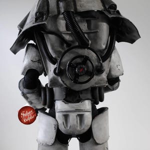 May include: A gray and black power armor suit with a large, round, black air filter on the chest. The suit has a large, gray helmet with a black visor. The suit is standing on a white background.