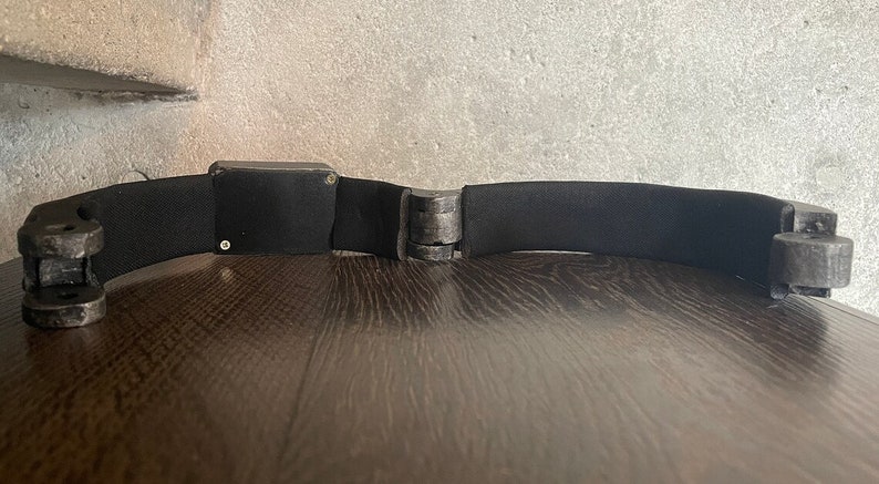 May include: A black headband with a rectangular black sensor in the middle. The headband is made of a soft, flexible material and has adjustable straps.