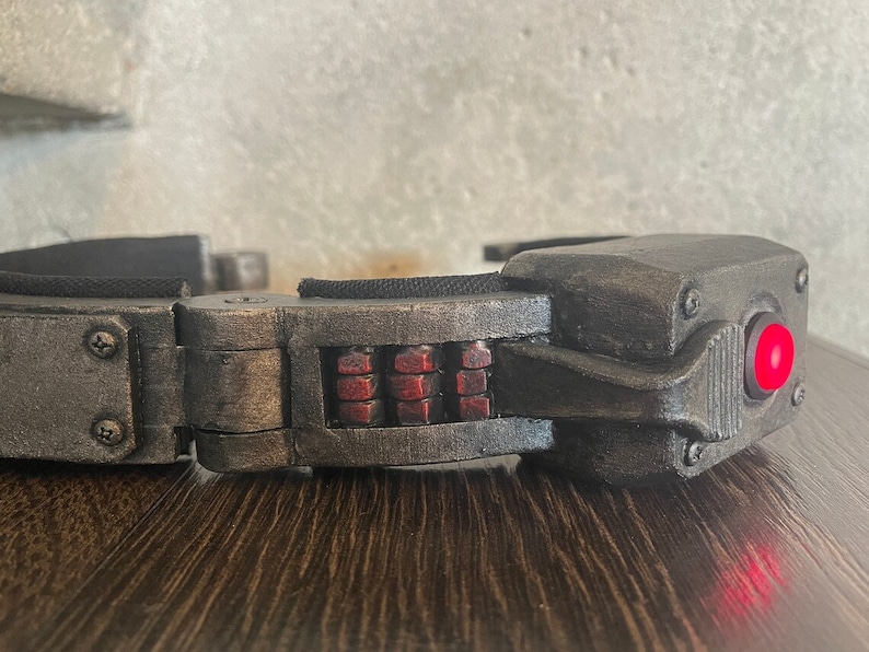 May include: A black and silver futuristic-looking device with a red light. The device has a series of small, rectangular, red lights on the front.