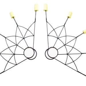 May include: Pair of black fire fans with a geometric design. Each fan features a circular handle and multiple spokes ending in yellow wicks. The fans are symmetrical and designed for performance or entertainment.
