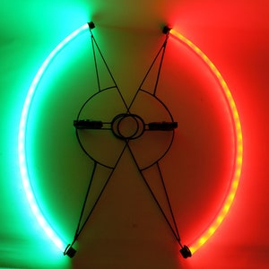 Pode incluir: Um par de luzes para rodas de bicicleta, uma verde e uma vermelha, montadas em uma estrutura de metal preta. As luzes são curvas e criam uma forma de semicírculo.