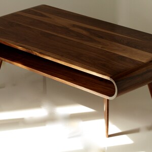 May include: A dark brown wooden coffee table with a curved, open shelf and tapered legs. The table has a natural wood finish.