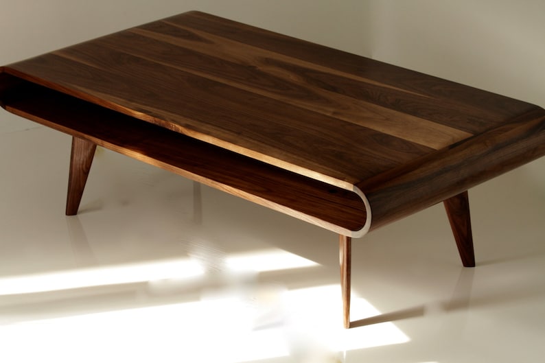 May include: A dark brown wooden coffee table with a curved, open shelf and tapered legs. The table has a natural wood finish.
