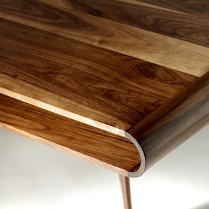 May include: A wooden coffee table with a curved edge and a lower shelf. The table is made of walnut wood and has a natural finish.